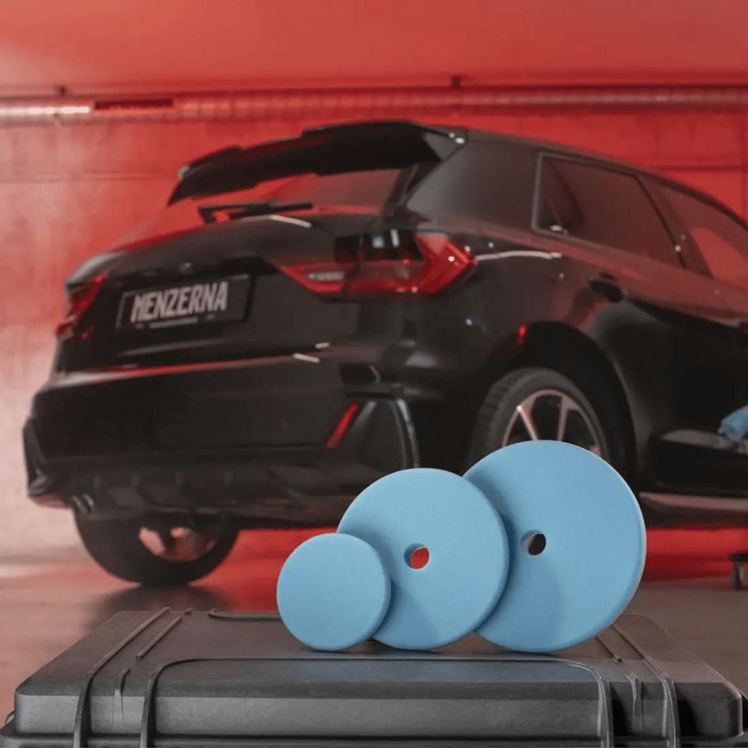 Drei Menzerna Premium Wax Foam Pad Polierpads vor einem Auto