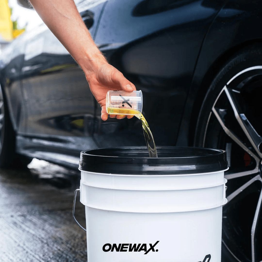 OneWax Just Clean Car Shampoo wird in einen Eimer gegossen von einem Messbecher