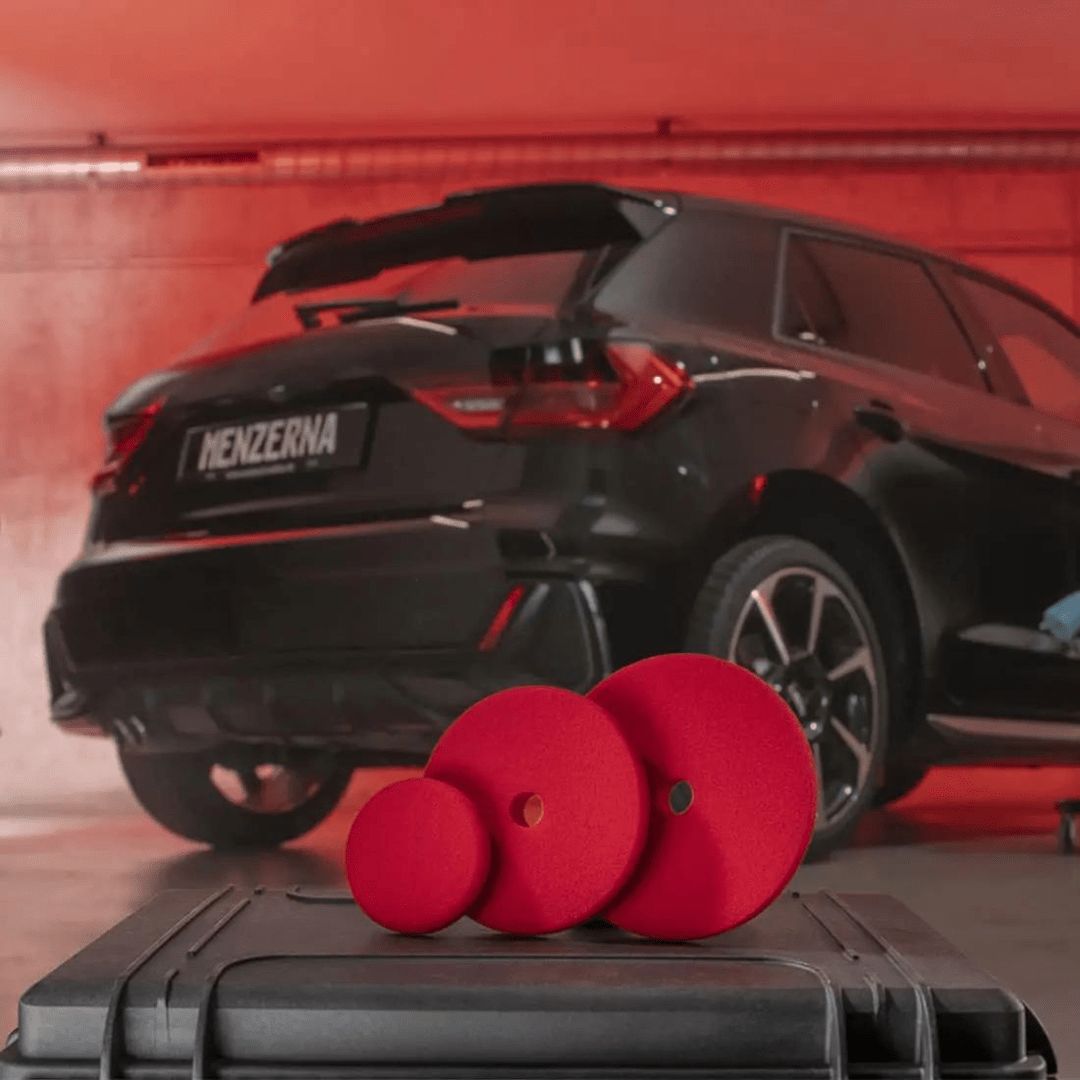 Drei Menzerna Heavy Cut Foam Pad Polierpads vor einem Auto