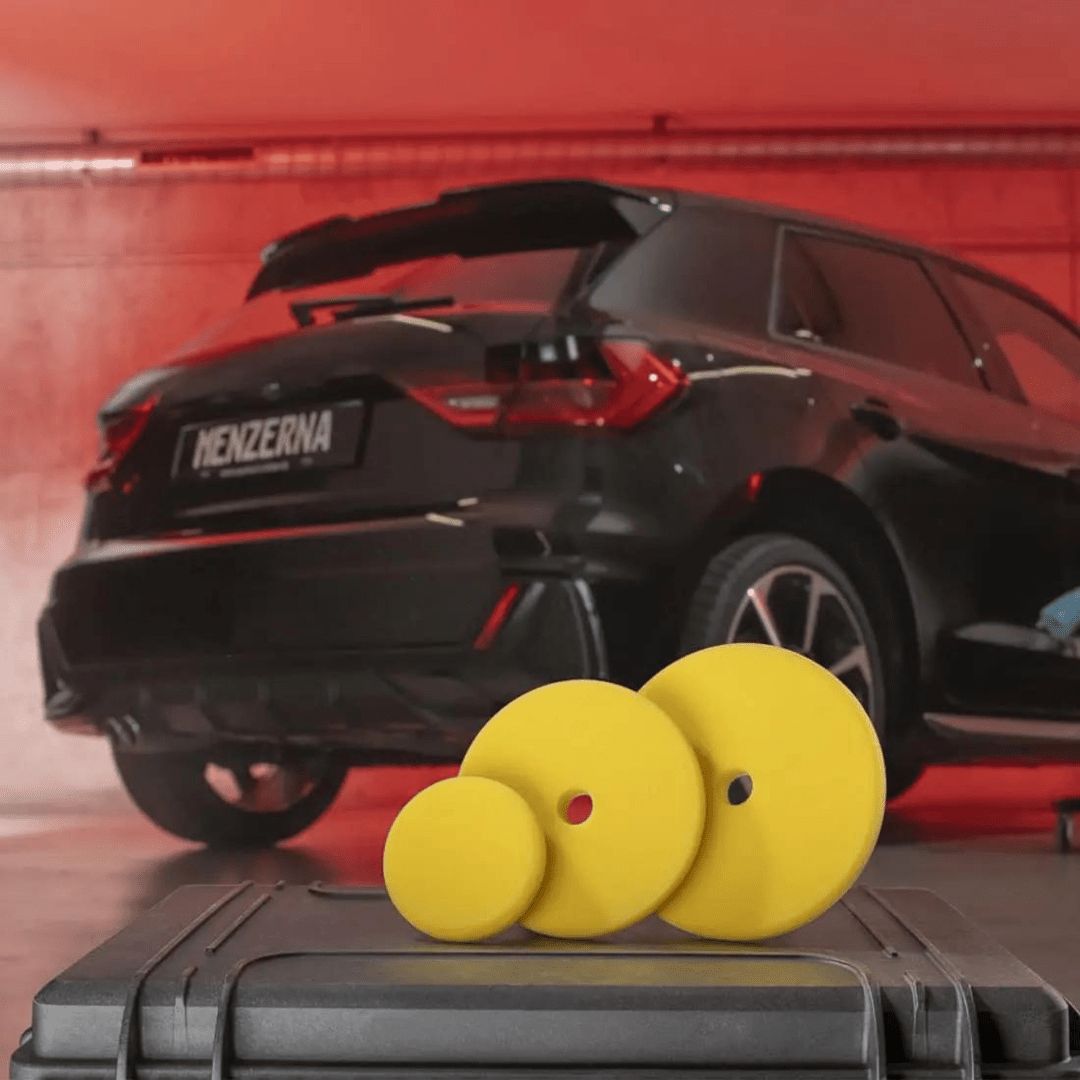 Drei Menzerna Medium Cut Foam Pad Polierpads vor einem Auto