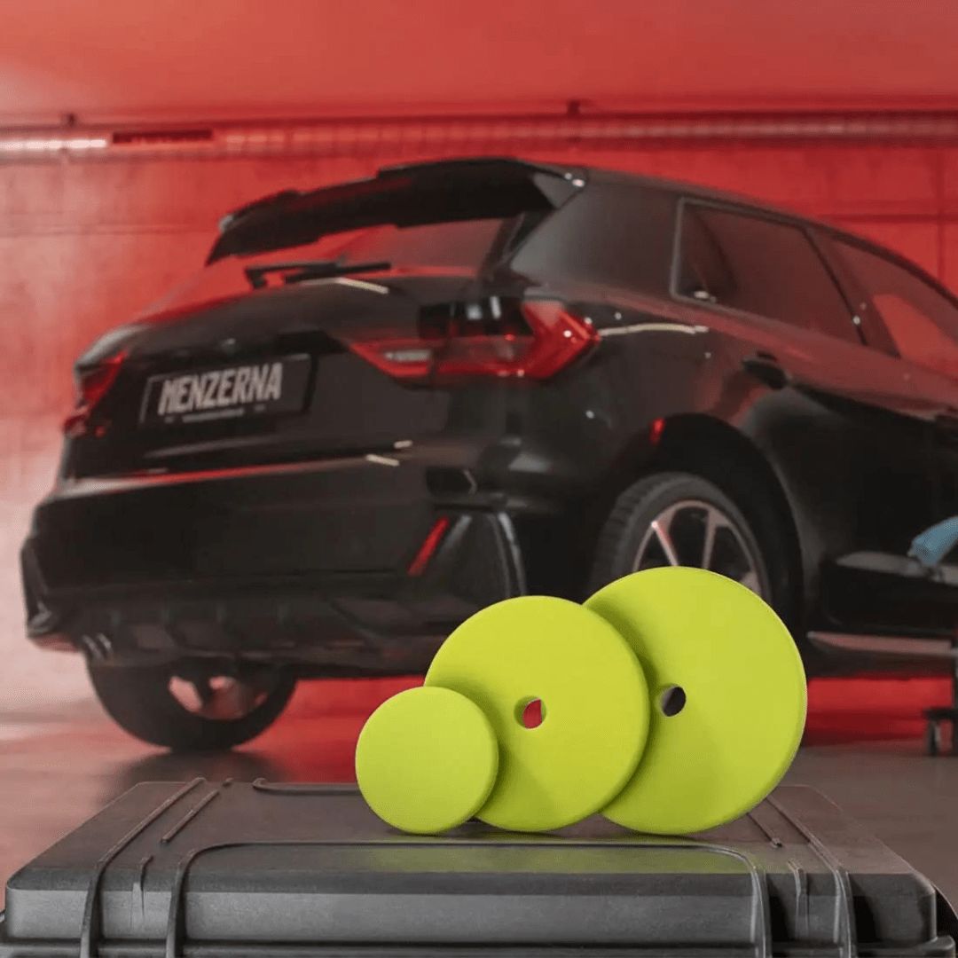 Drei Menzerna Soft Cut Foam Pad Polierpads vor einem Auto