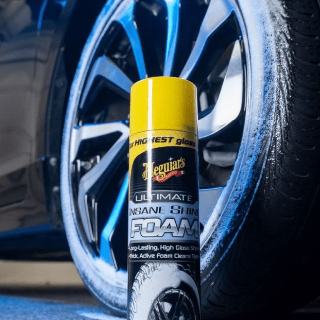 Die Meguiars Ultimate Insane Shine Foam Reifenpflege Sprühdose vor einem Reifen mit weissem Schaum