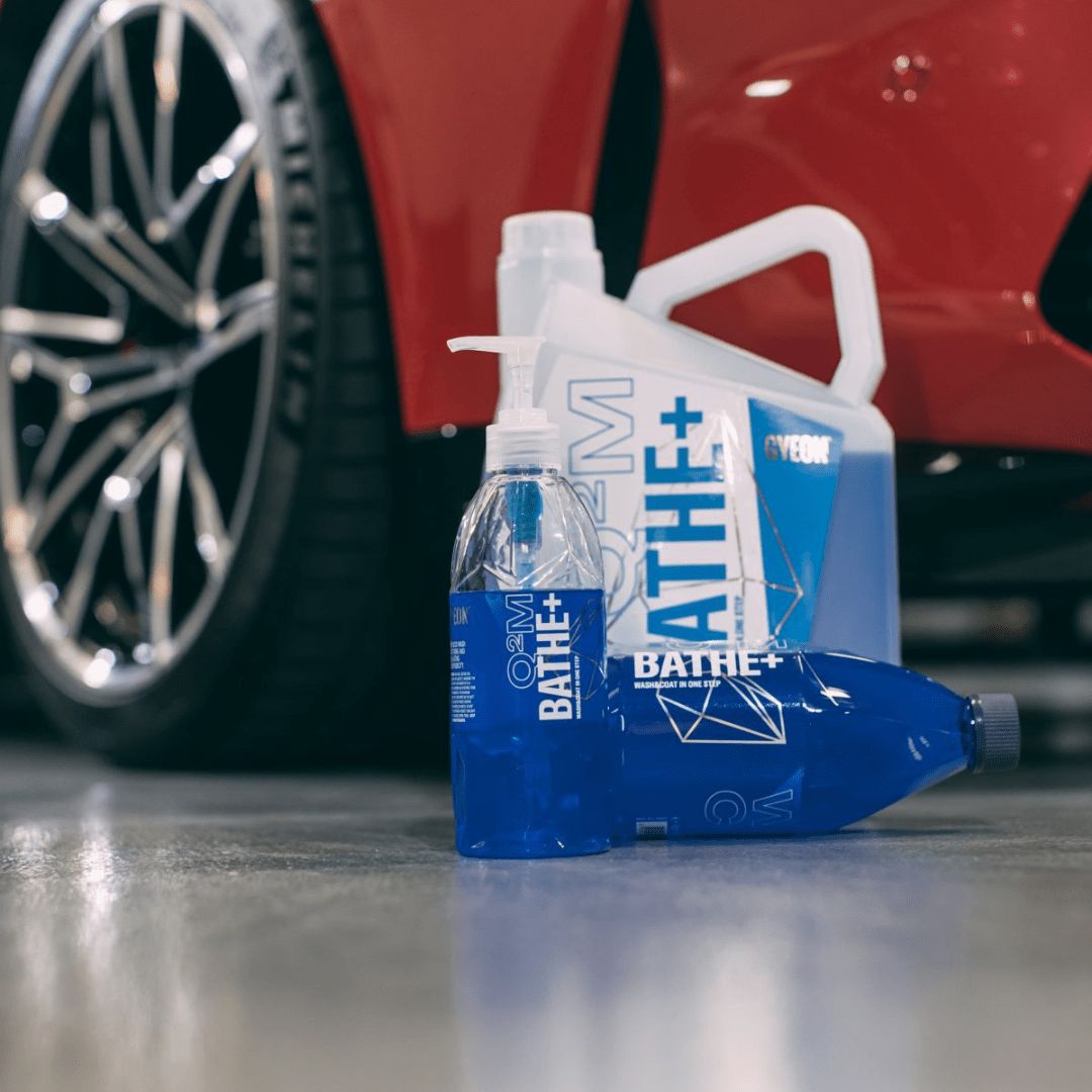 Die verschiedenen Grössen der Gyeon Q²M Bathe+ Autoshampoo Flaschen vor einem Auto